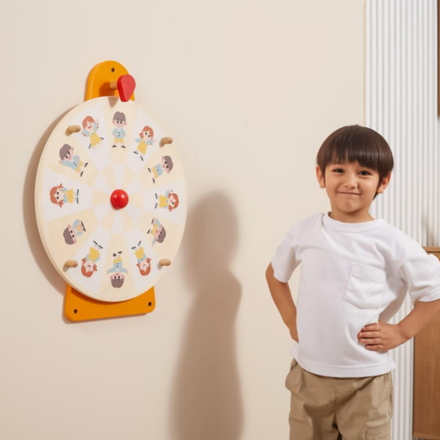 Child standing next to a colorful wall game with cartoon characters on a beige wall.