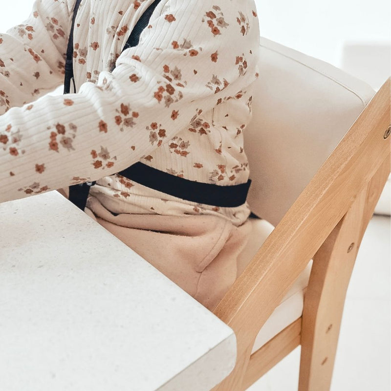 Child wearing a floral shirt sitting on a white chair with a wooden armrest.