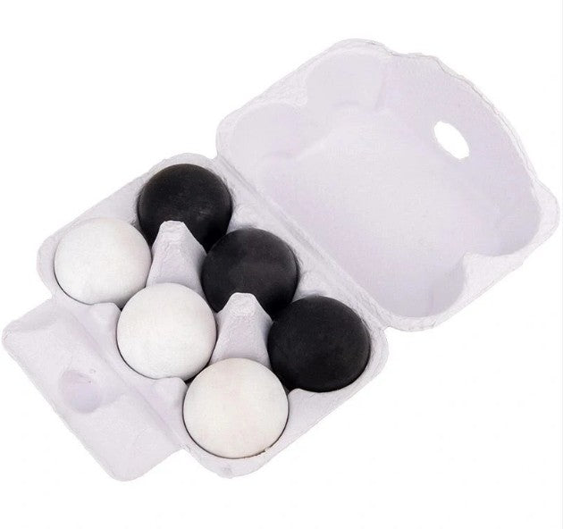 A white styrofoam egg carton holding six eggs, four black and two white, photographed on a plain white background.